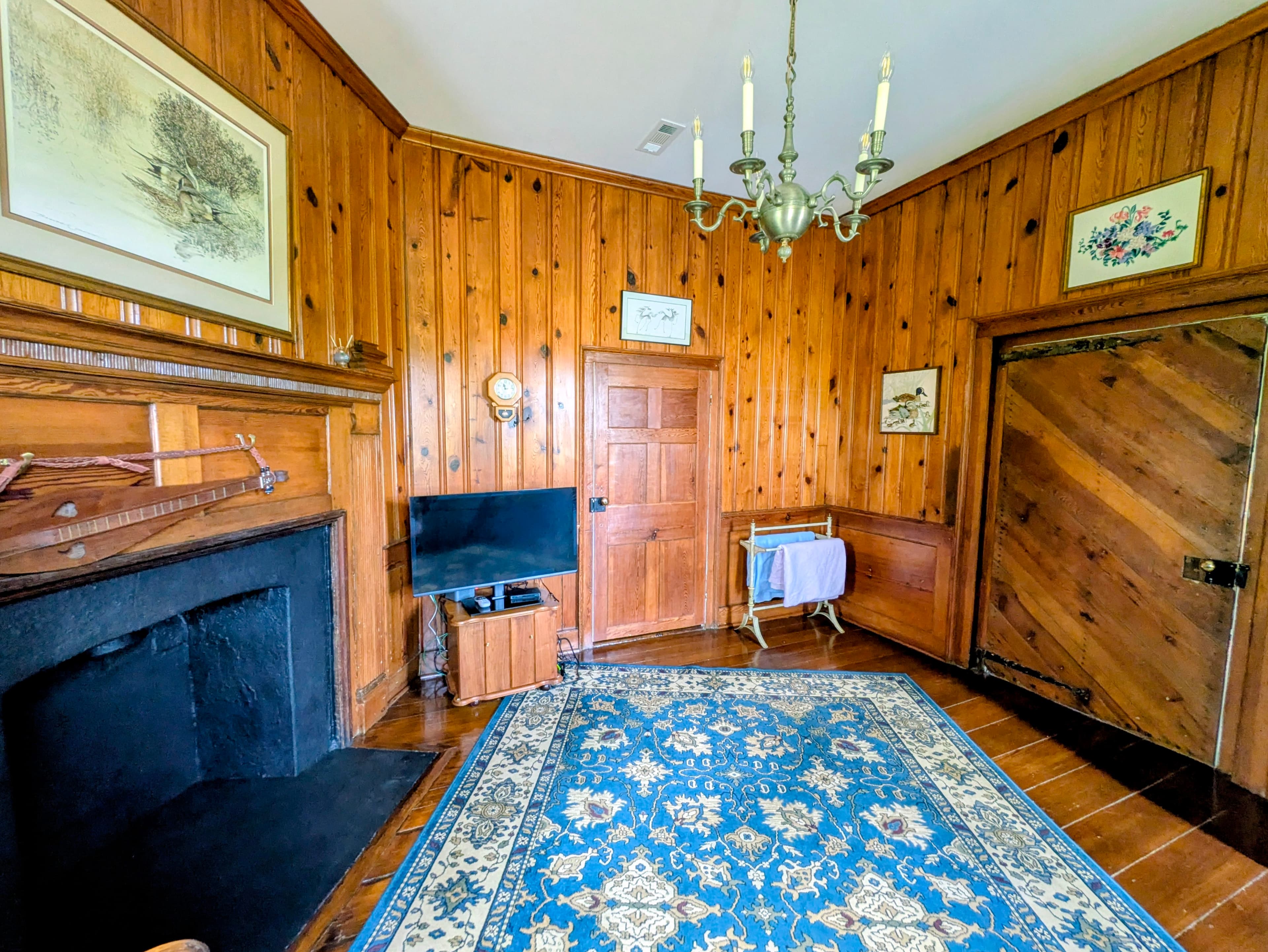 In sitting area room looking toward closed door to the bedroom, with entrance door to the right. Blue rug, TV, fireplace