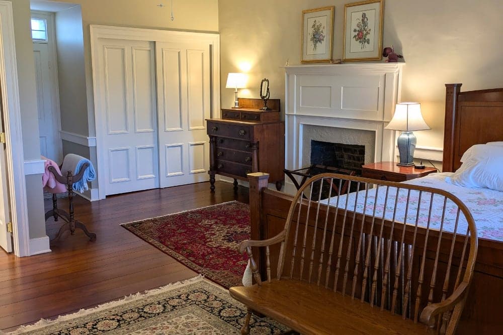Cozy bedroom featuring a wooden bed, a dresser, a fireplace, and a vintage-style chair on a patterned rug.