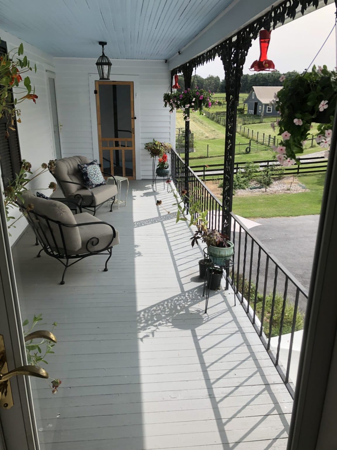 Private balcony overlooking the lawn and farm, with two large chairs, hanging plants, and potted plants