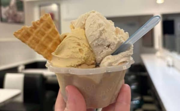 A hand holding a cup of ice cream with three different flavors and a waffle cone.