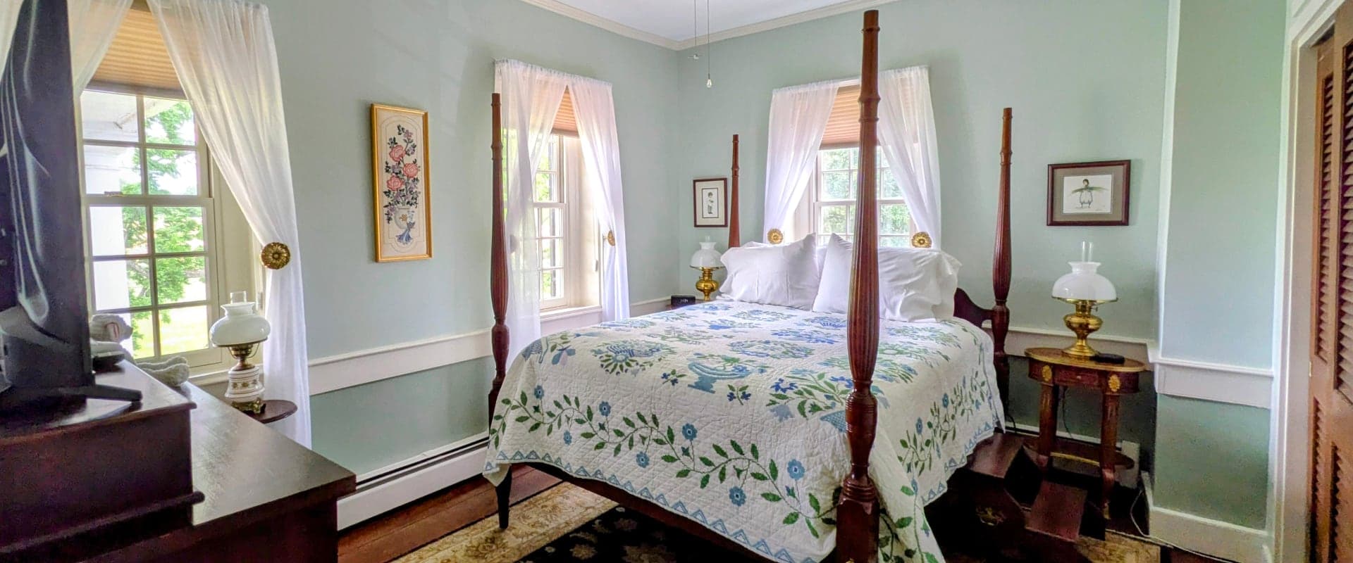 A cozy bedroom with a four-poster bed, floral quilt, and light green walls.