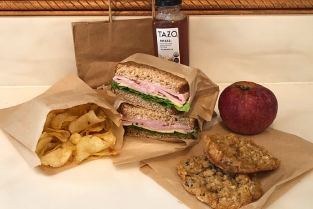 A sandwich with lettuce and turkey, chips, an apple, and cookies beside a beverage on a countertop.