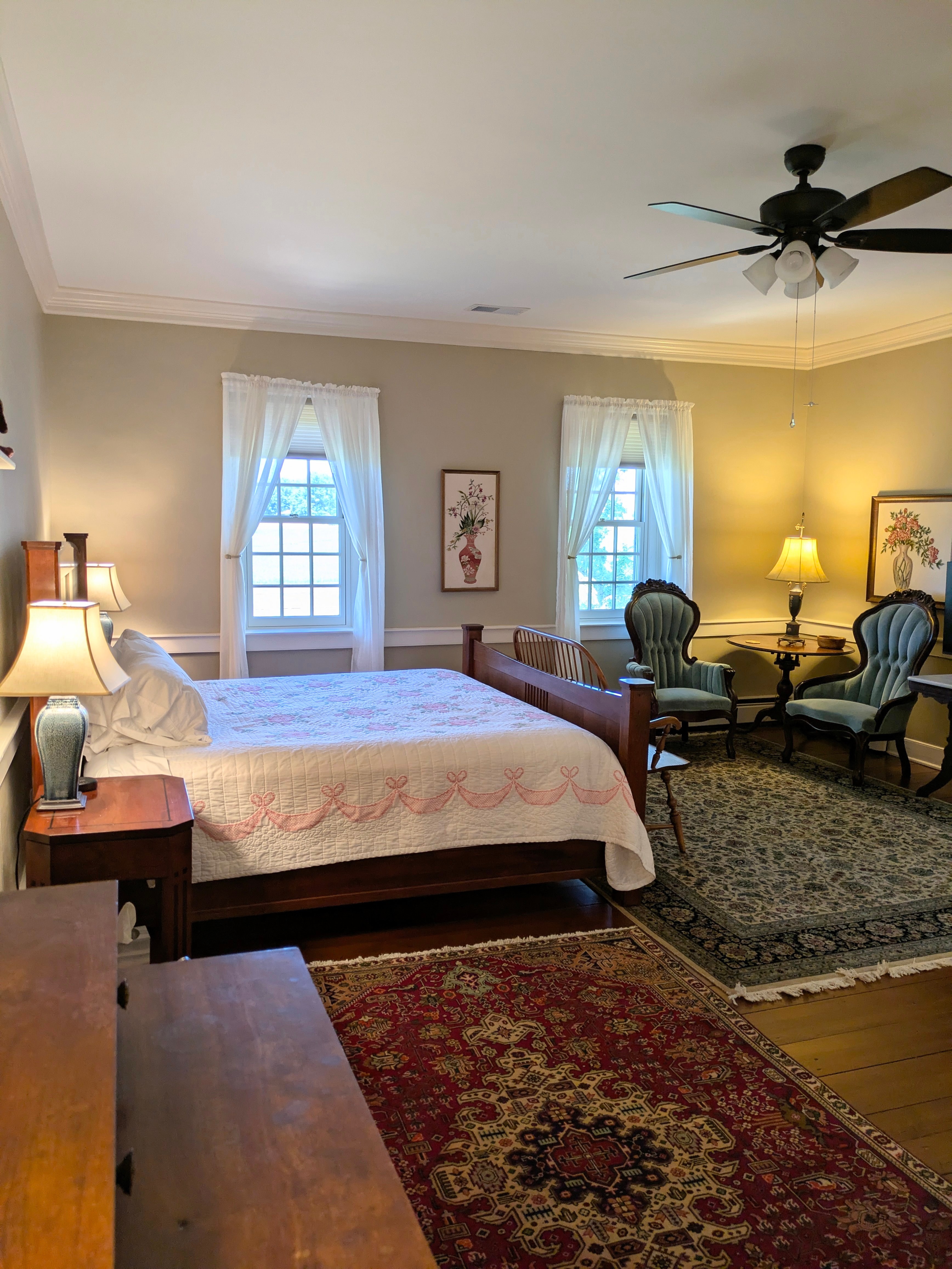 King bed, two victorian chairs, endtable with lamp, two windows, oriental rugs