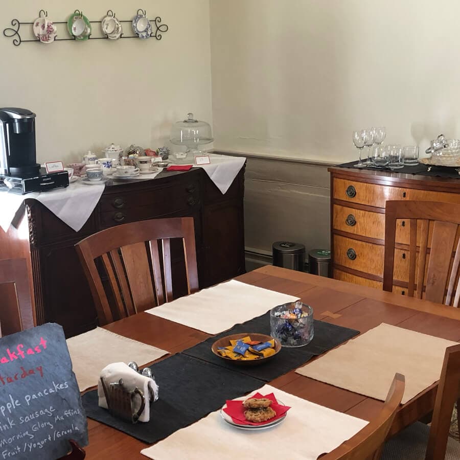 A cozy breakfast setting featuring a wooden table, dining chairs, and a sideboard with dishes and a coffee maker.