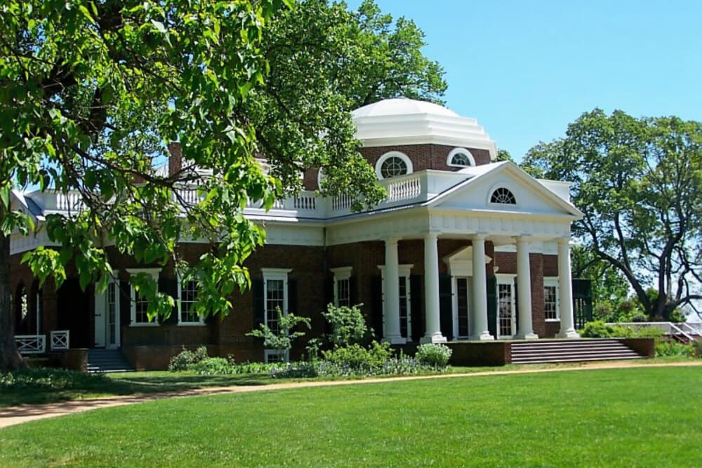 A historic brick building with a white domed roof, surrounded by lush greenery.