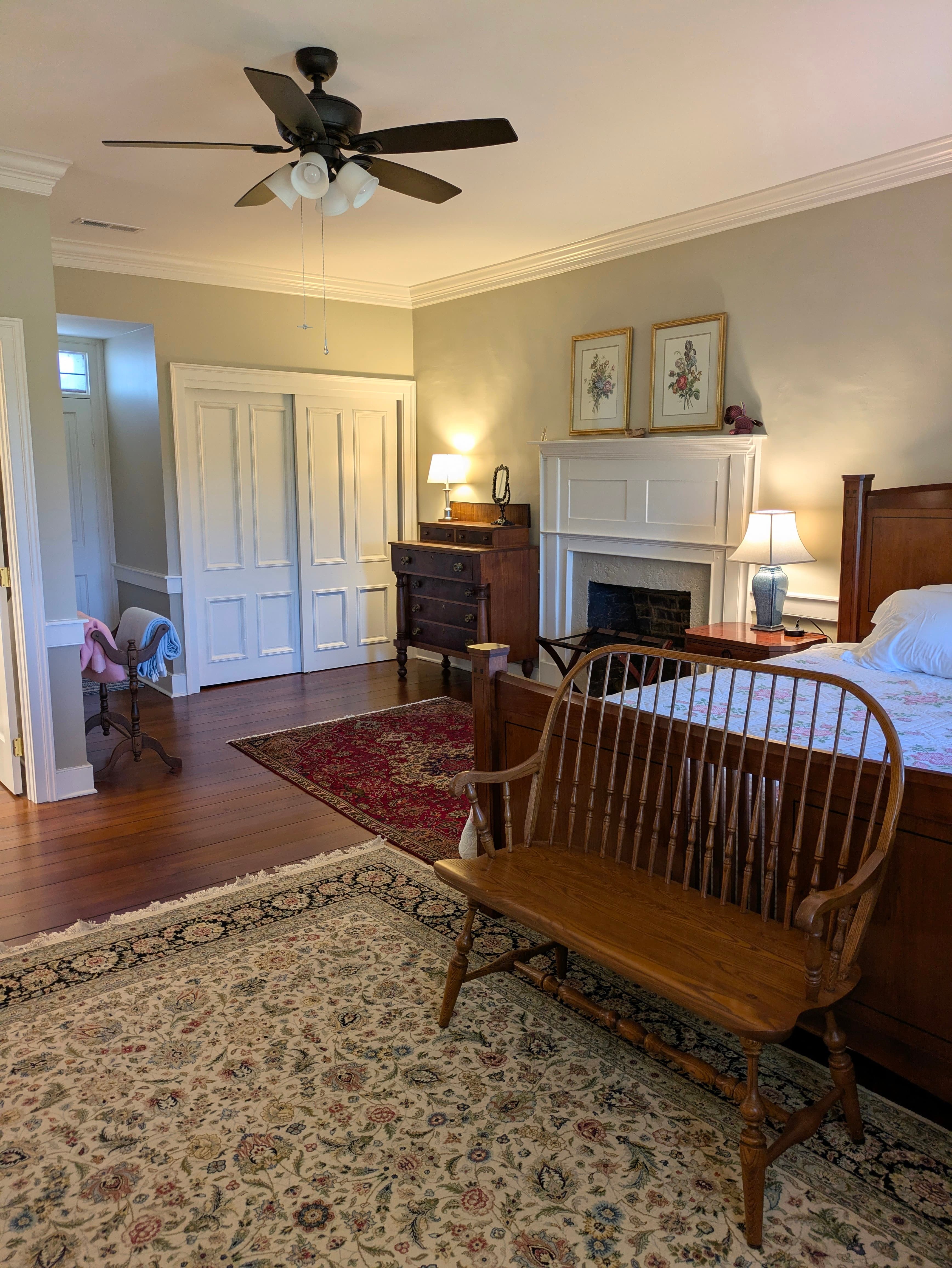 View from sitting area with king bed, parson's bench, oriental rugs, dresser, fireplace with mantel, closet