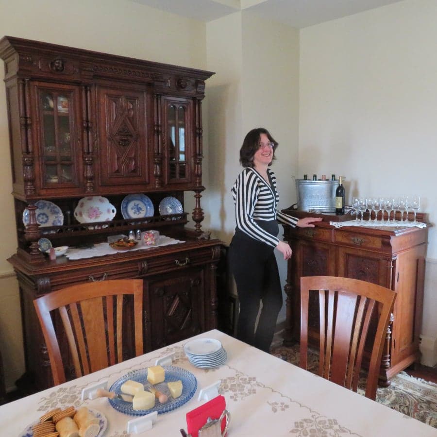 A woman in a striped shirt stands by a wooden bar cabinet in a warmly decorated dining room, with a table set for a meal.