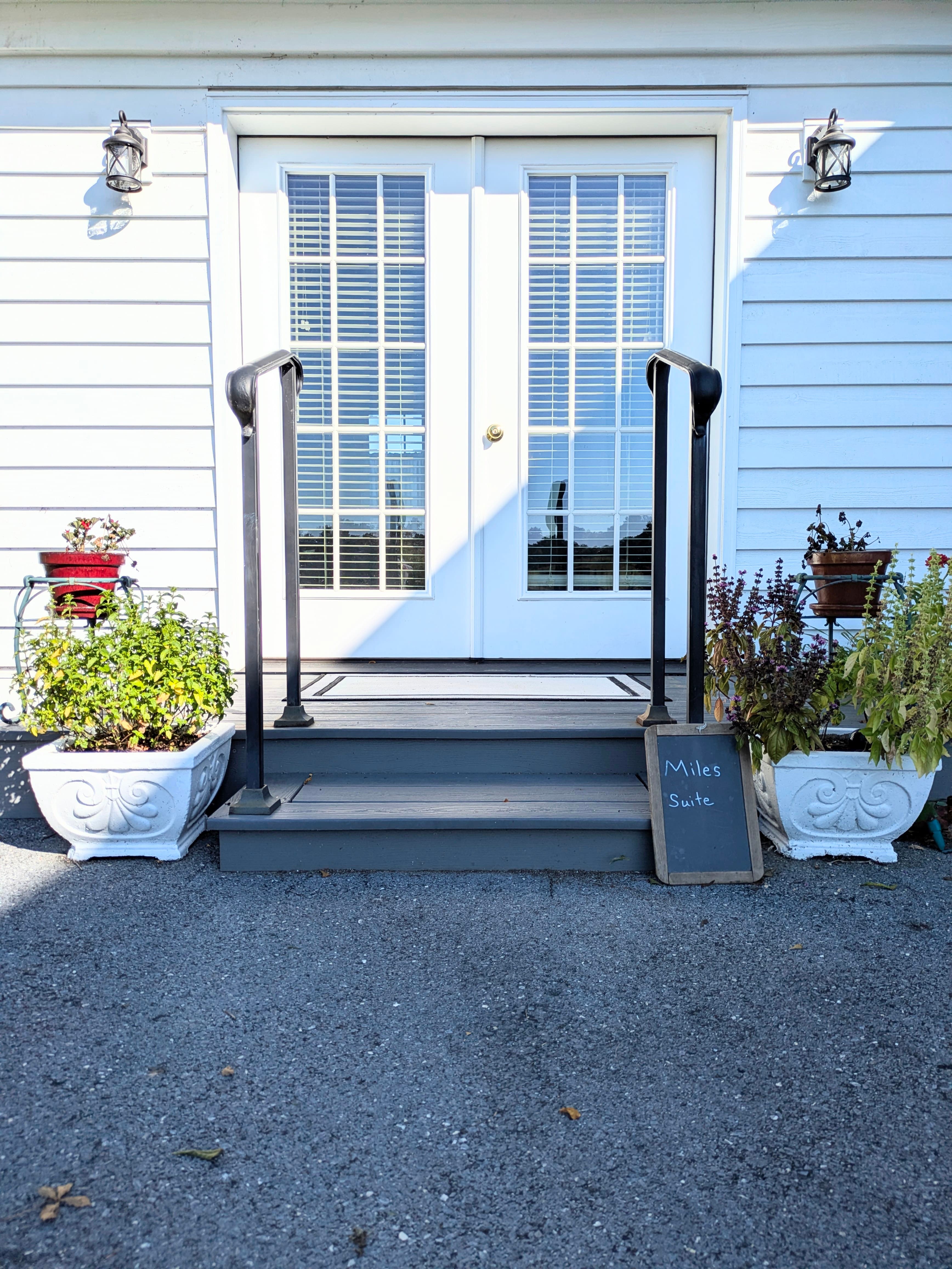 View of external entrance from private parking spot with porch lights, two shallow steps, and railings