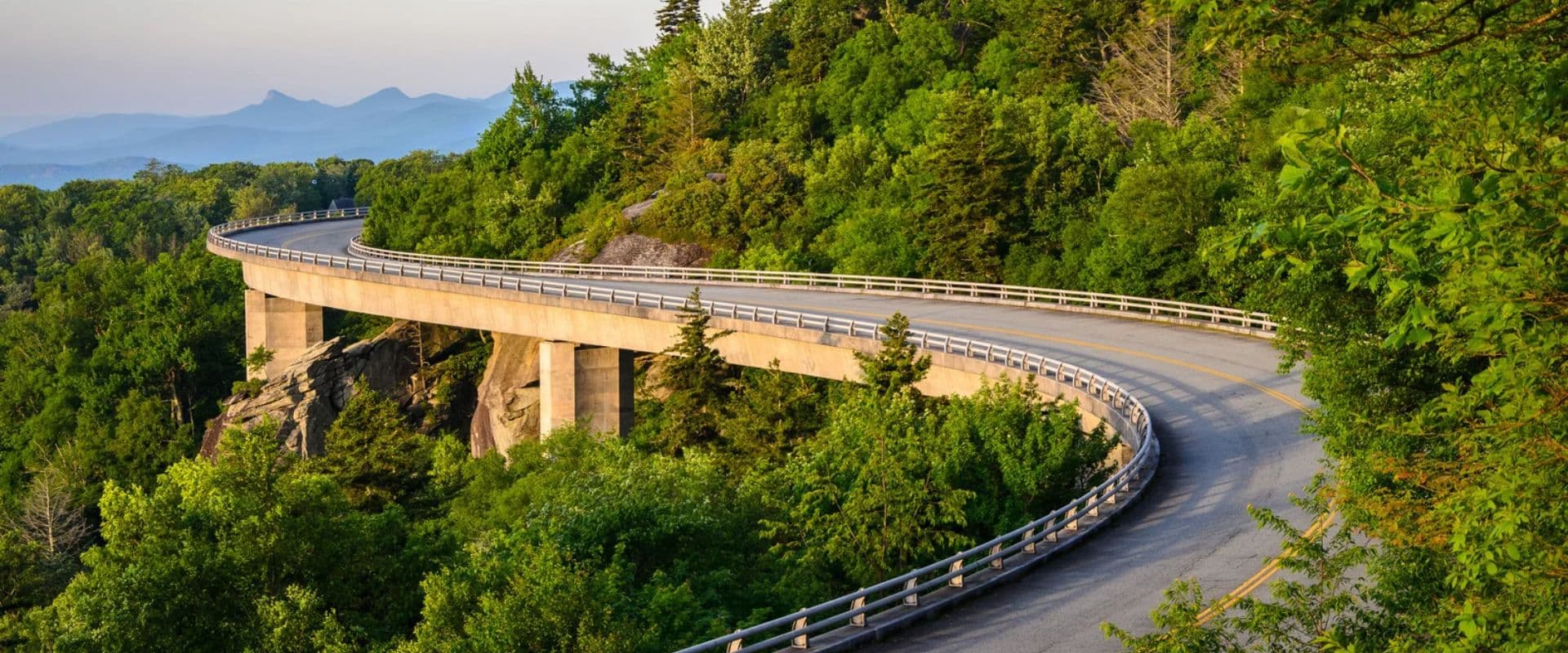A winding road curves through lush greenery with mountains in the background.
