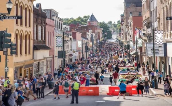 A bustling street filled with crowds and colorful barriers, lined with historic buildings under a bright sky.