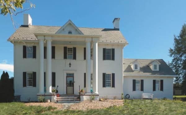 A large, stately white house with columns and black shutters under a clear blue sky.