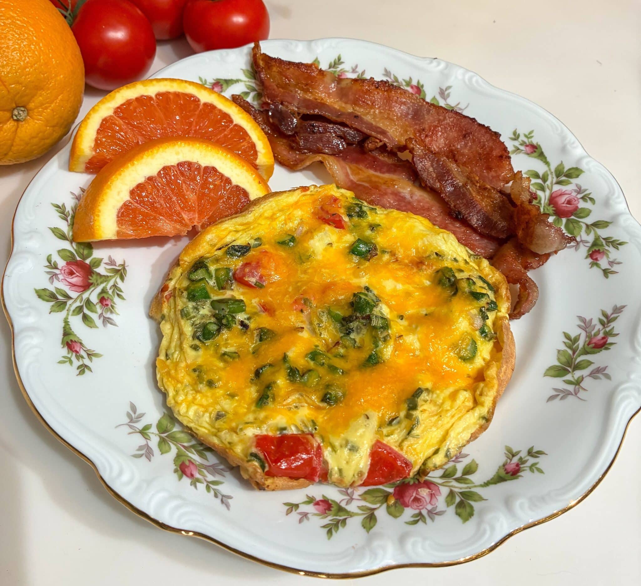 A plate featuring a colorful vegetable omelet, crispy bacon, and orange slices.