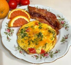 A plate with a cheese and vegetable omelet, crispy bacon, and orange slices, accompanied by cherry tomatoes.