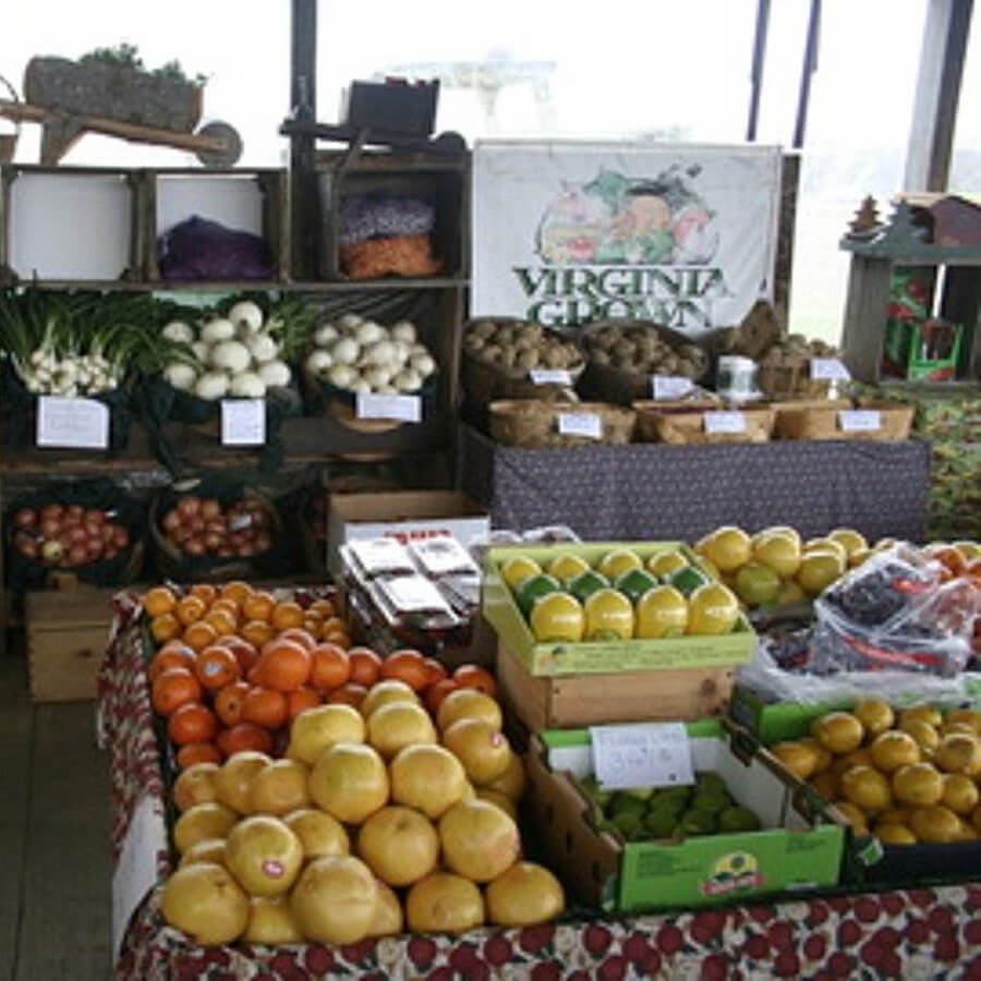 A farm stand displays a variety of fruits and vegetables, including citrus, apples, and potatoes, under a "Virginia Grown" sign.