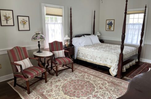 Bedroom with 4-poster bed, oriental rug, two windows, two chairs with an endtable