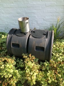 Black two-bin composting barrel, with a steel kitchen compost can sitting on it.