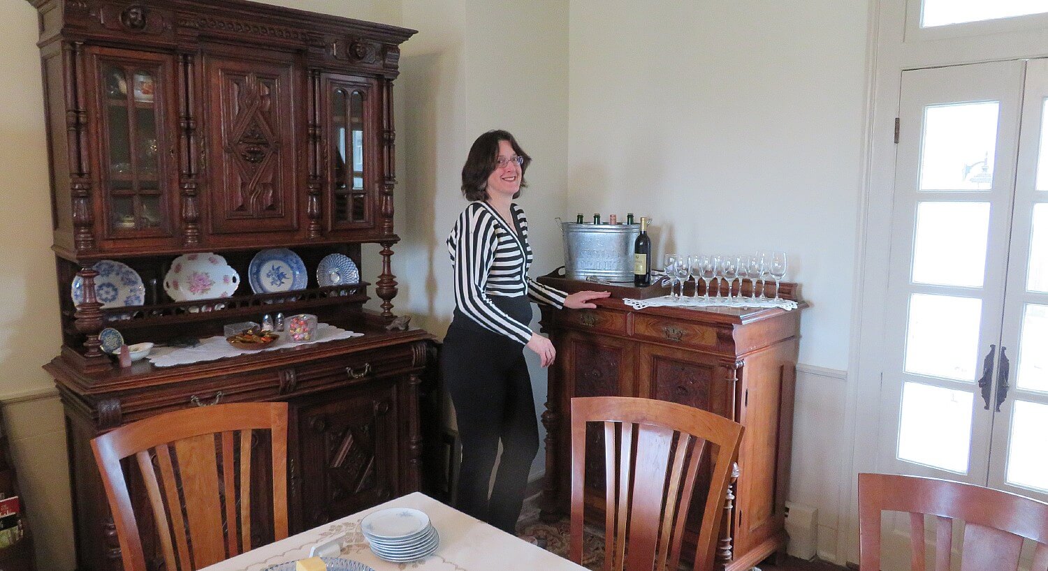 Woman in black pants and striped shirt standing next to a tall buffet table in a dining room