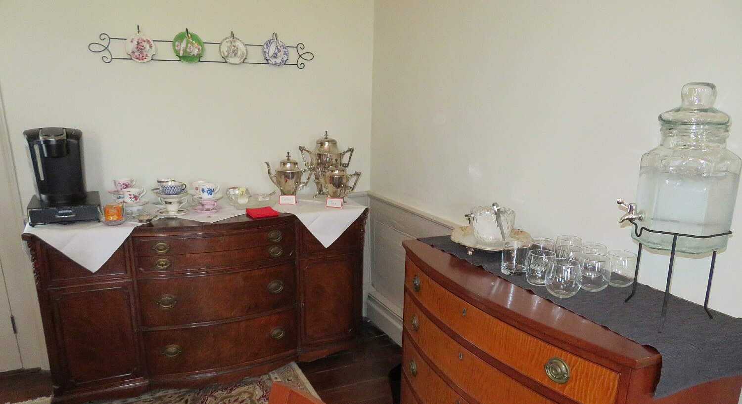 Corner of a dining room showing two dark wood buffet tables holding coffee and water drinkware