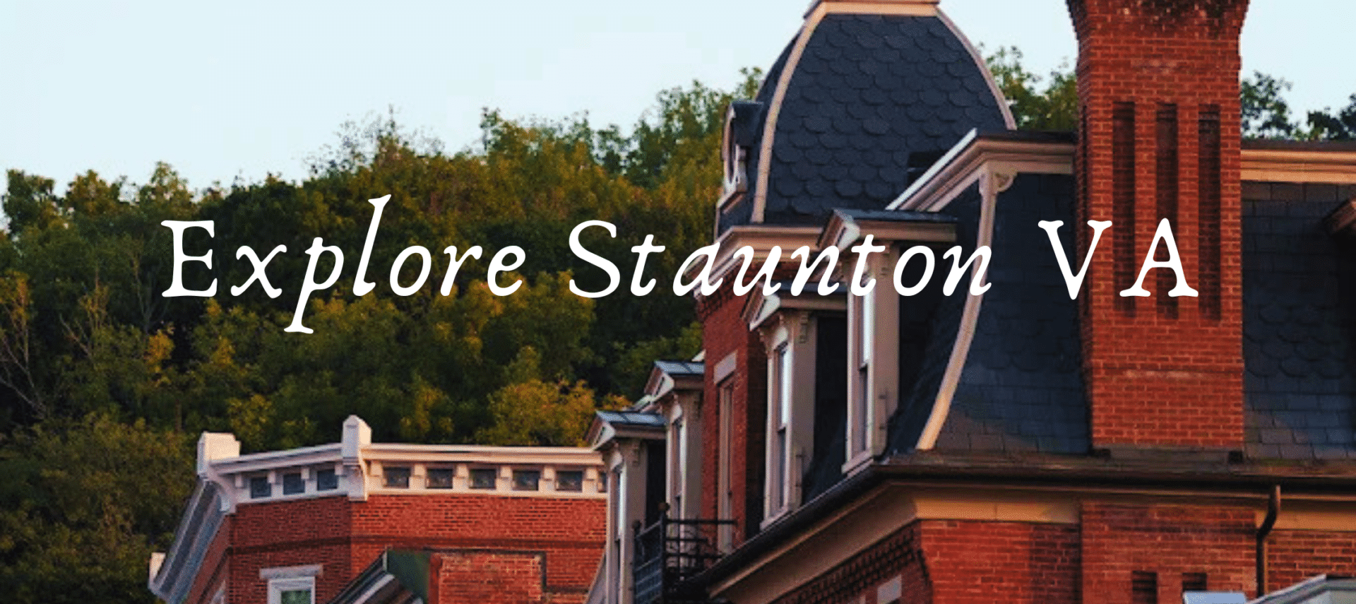 Brick row houses with a slate roof and a banner across the facade that says 'Explore Staunton VA' over a tree-lined backdrop.