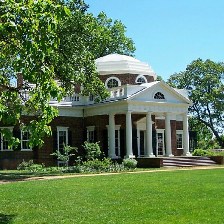 Elegant historic brick home with large front porch with white columns and expansive green lawn