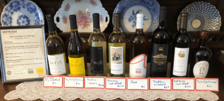 Eight bottles of wine on a breakfront with labels in front of each with pricing and description.